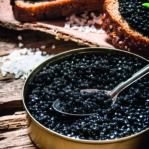 Sandwiches with black caviar, a jar of caviar and a spoon. On a wooden table.