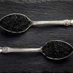 Two vintage silver spoons with black sturgeon caviar on black slate stone background. Top view, flat lay, copy space
