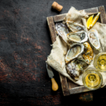 Raw oysters on a rag in a wooden tray with glasses of white wine. On dark rustic background